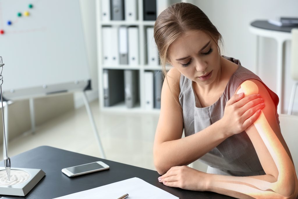 Young woman suffering from pain in shoulder at workplace